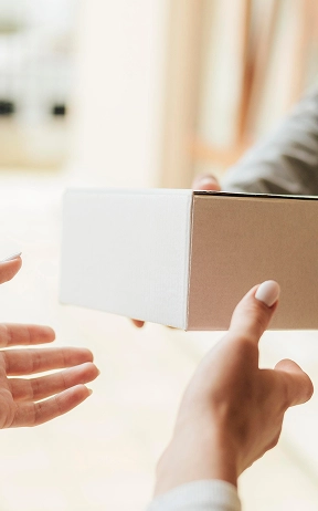 Iemand overhandigt een wit pakket aan een ander, wat symbool staat voor de bezorging of de uitwisseling van een geschenk. De omgeving is licht en luchtig, wat een gevoel van verwachting oproept.